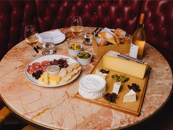 A charcuterie platter and cheeseboard with glasses of rose laid out on a table near a red banquette.