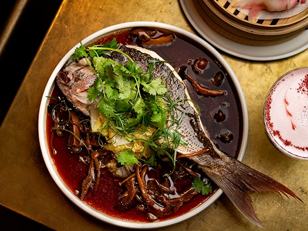 A whole baked fish at Pearl Dining pictured on a plate with chillis and coriander.