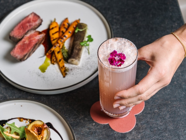 a hand holding a drink with food on the table at The Lex