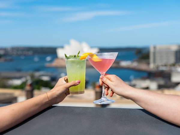 clinking cocktail glasses against a backdrop of the Sydney Harbour, YHA Rooftop Bar