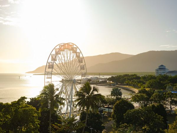 Golden hour over the ferris wheel, treetops, lagoon and hilly backdrop of the esplanade at Cairns - Coral Sea, Cairns; Far North Queensland, Australia