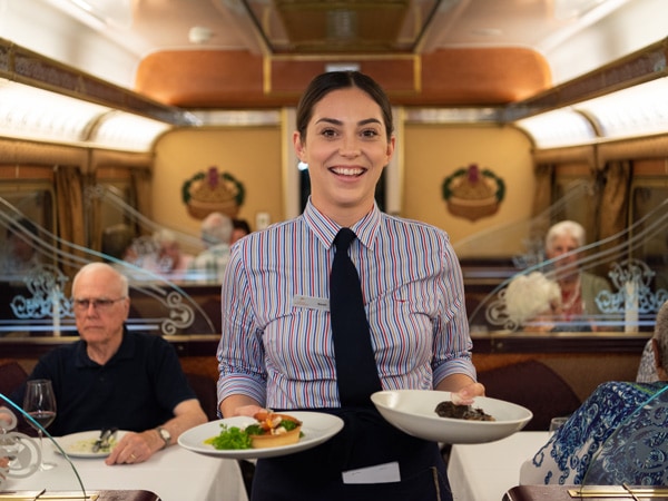 a staff of an Art Deco-inspired Queen Adelaide dining car holding plates of food