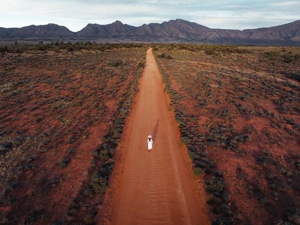 a drone shot of a woman walking in the middle of the road at Ikara-Flinders Ranges National Park