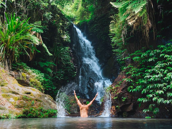 a man raising his hands in the air while dipping in a waterfall at Lamington National Park