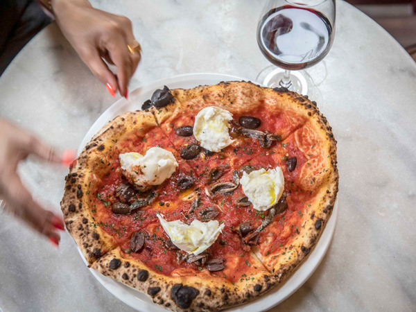 a hand slicing pizza at Puttanesca Osteria, Italian restaurants Melbourne