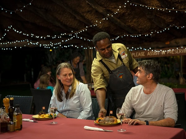 a man serving food to the couple at the restaurant of Curtin Springs Wayside Inn