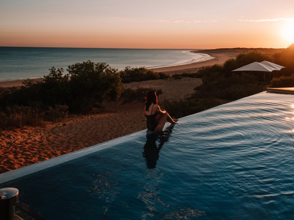 a woman sitting on the edge of the infinity pool at Eco Beach Resort, WA during sunset