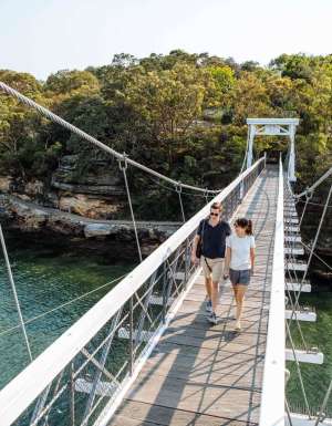 A couple cross the suspension bridge at Parsley Bay while walking the Bondi to Manly coastal walk
