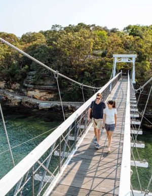 A couple cross the suspension bridge at Parsley Bay while walking the Bondi to Manly coastal walk