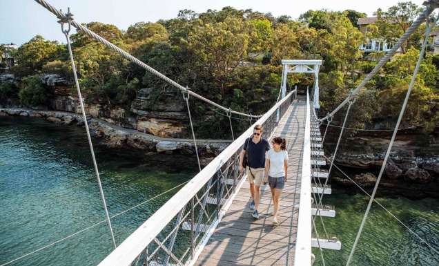 A couple cross the suspension bridge at Parsley Bay while walking the Bondi to Manly coastal walk