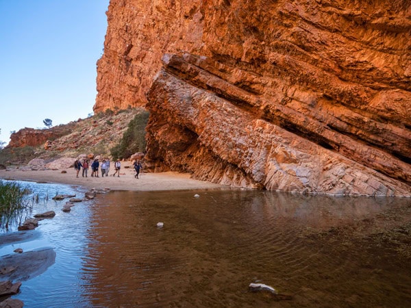 a group hiking across a scenic gorge and waterhole along Larapinta Trail