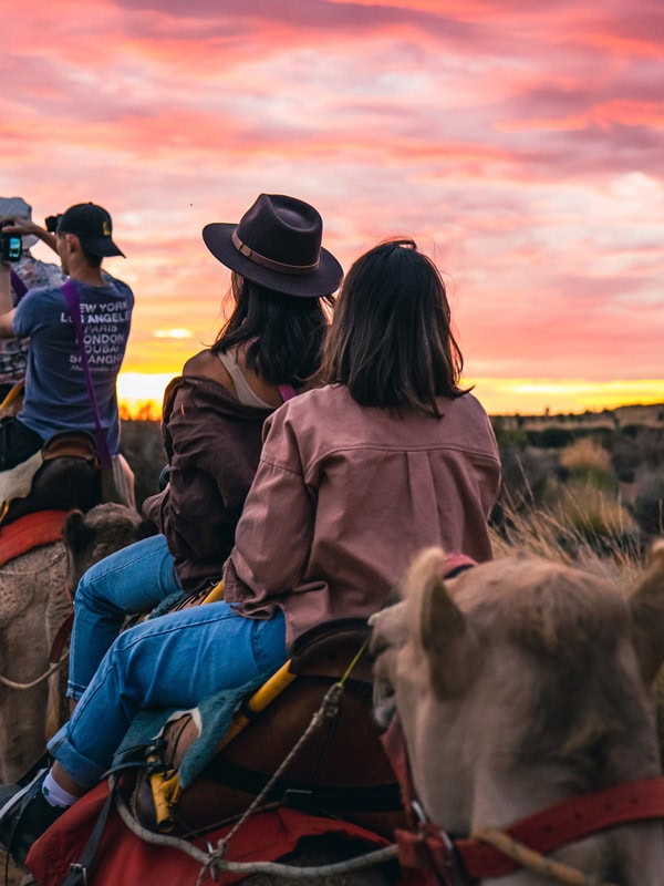 people riding camels at sunrise in Uluru
