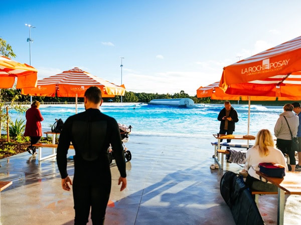 people sitting at the poolside area under the umbrellas at URBNSURF Sydney 