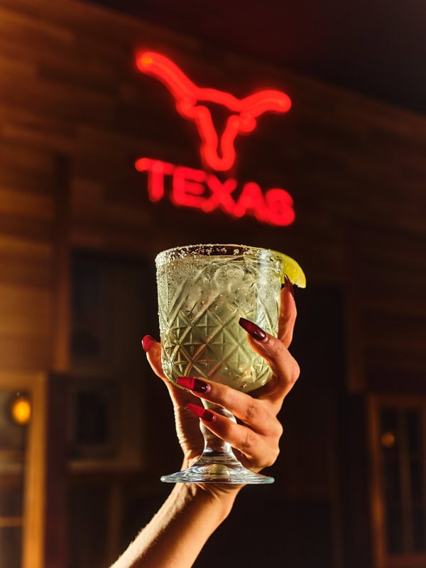 a hand holding a green drink against a Texas sign at Honky Tonk