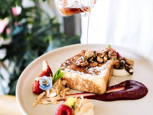 drizzling sweet sauce over a plate of dessert at Little French Nest