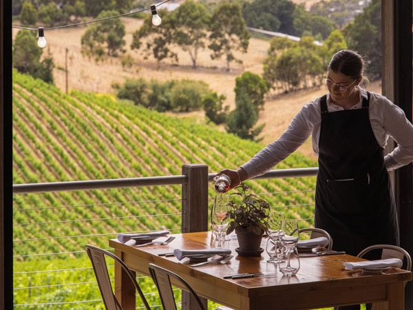 a server at Mount Lofty Ranges Vineyard Restaurant preparing the table fronting scenic valley views