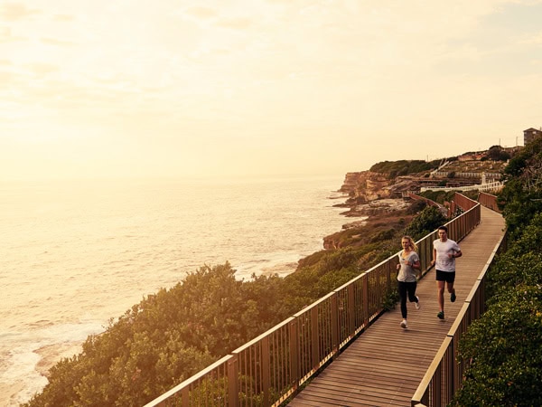 two people jogging along an elevated boardwalk with views of the ocean