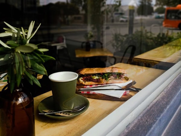 a cup of coffee and sandwich on a table by the glass window at Quasimodo’s Cafe