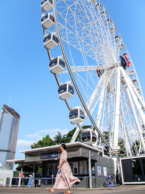 a woman walking in front of The Wheel of Brisbane, South Bank Parklands