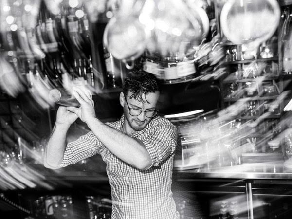 a black and white photo of a bartender shaking up drinks at Bar Stelo