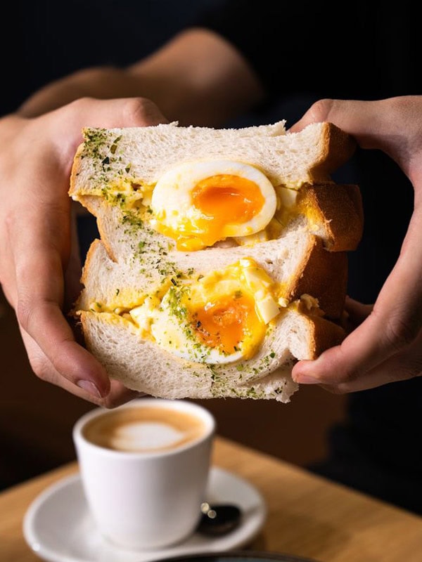 a hand holding an egg sandwich with coffee at Yuna Restaurant and Café