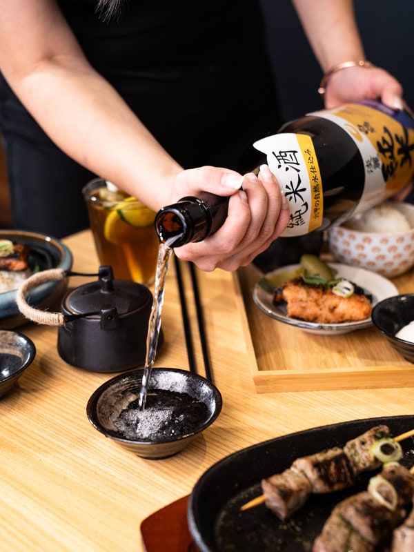 a hand pouring a bottle of sake at Yuna Restaurant and Café