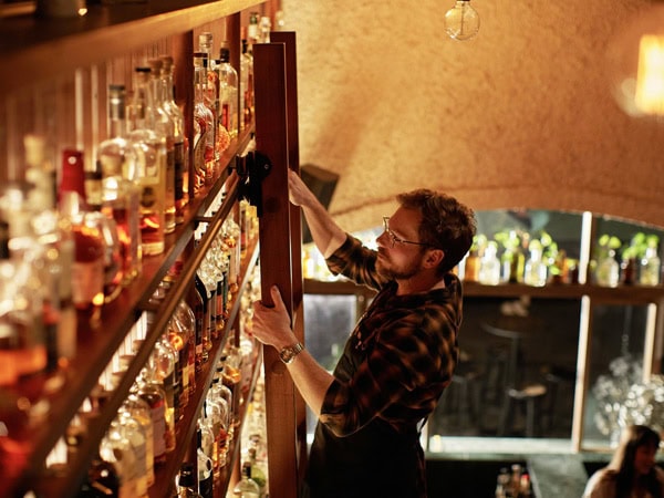 a bartender climbing up a sliding ladder to pull bottles from the top shelf at Malt & Juniper, Adelaide