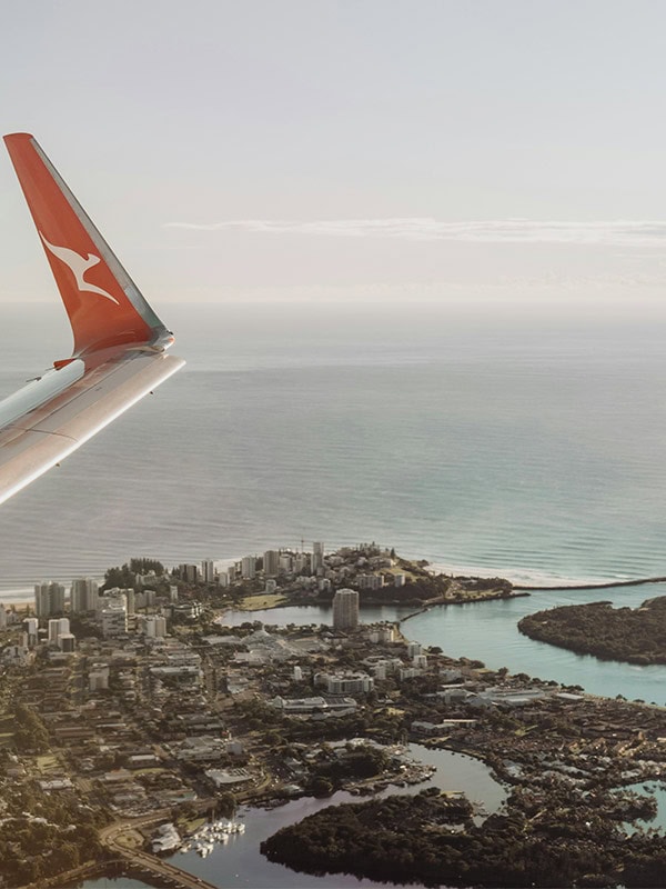 tip of qantas plane wing flying over australian city