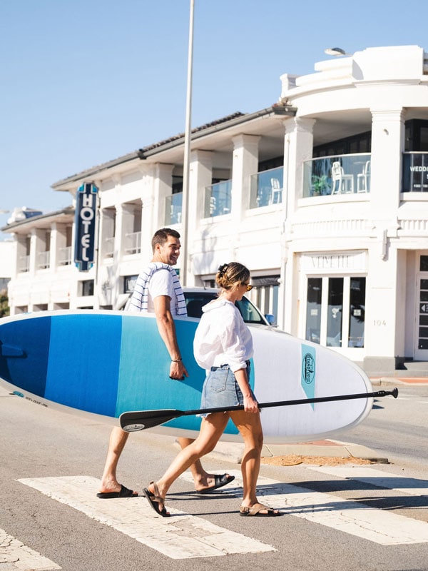 a couple with a surfboard outside The Cottesloe Beach Hotel, Perth