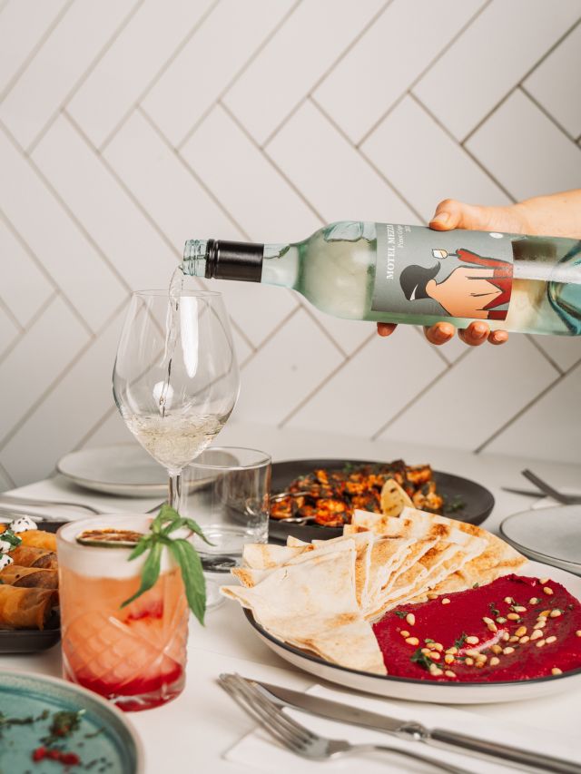 pouring a drink into a glass with Middle Eastern food on the table at Motel Mezza, Wyong