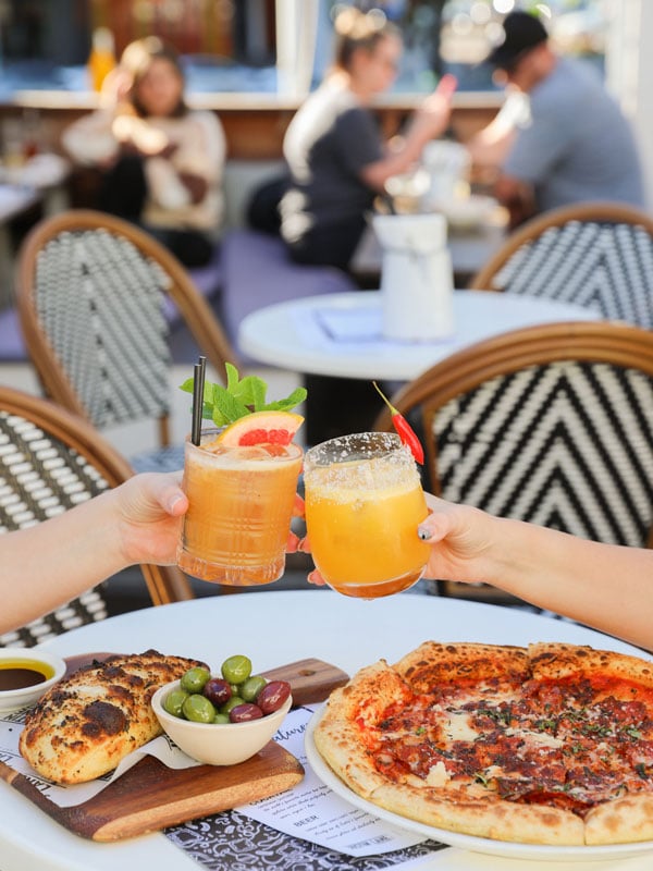 clinking drinks above pizza on the table at Justin Lane