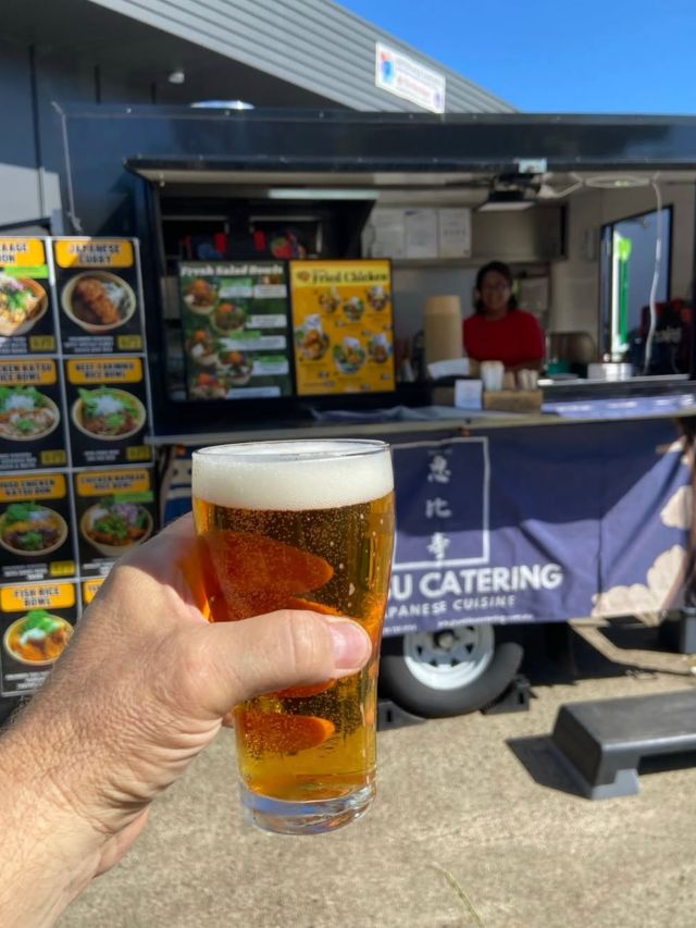 a hand holding a glass of Flat Lizard beer in front of Yebisu Catering food truck