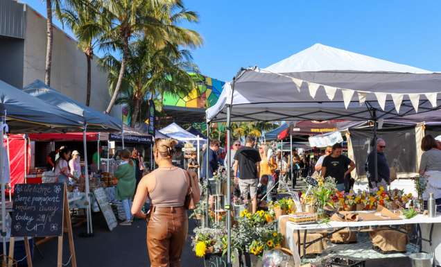 a woman walking in an outdoor market beside a flower stall, HOTA Farmers & Artisan Markets
