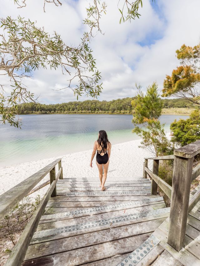 a woman walks down the wooden stairs to Lake McKenzie