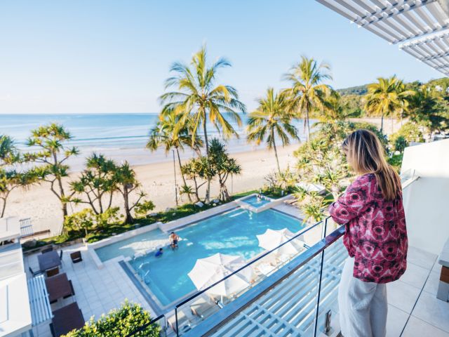 a woman on the balcony looks out to the pool and Noosa Main Beach at Fairshore Noosa