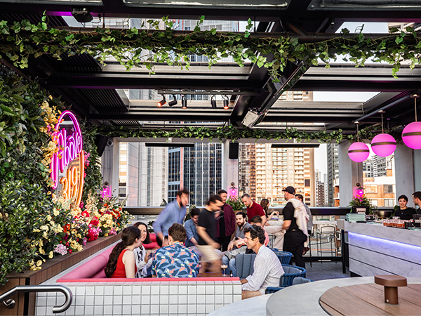Above 319 is an urban oasis atop the floor of Vibe Hotel Darling Harbour. Image shows outdoor seating and people standing near the bar.