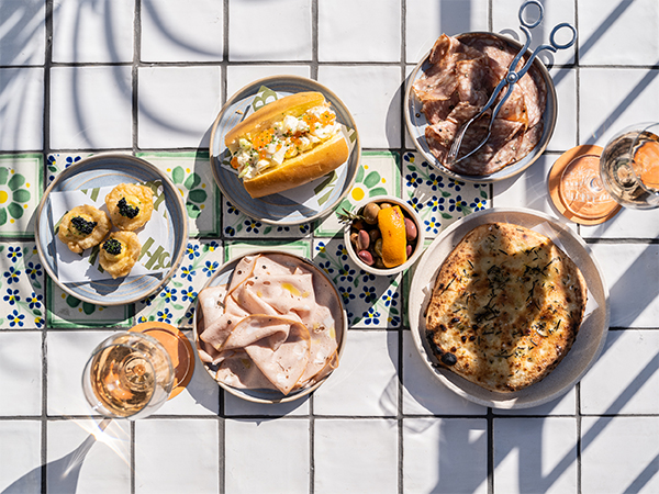 An array of decadent mezze-style dishes on offer on a table with shadows from the palm trees.