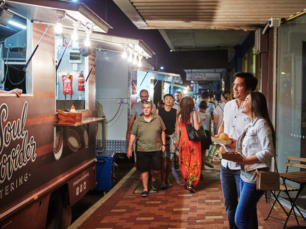 a couple eating in front of a food truck at Inglewood Night Markets