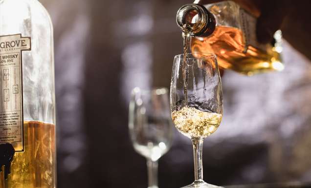 person pouring belgrove distillery whisky into a a glass of ice tasmania