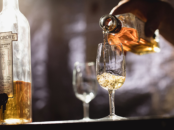 person pouring belgrove distillery whisky into a a glass of ice tasmania