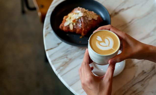 person holiding coffe and croissant in cafe