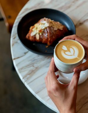 person holiding coffe and croissant in cafe