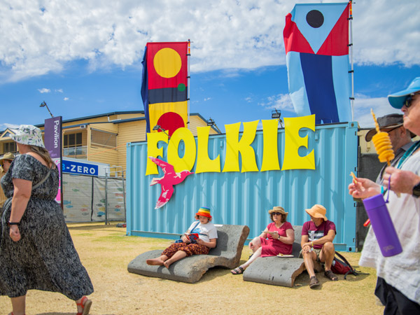 visitors sitting under The Folkie signage, Port Fairy Folk Festival