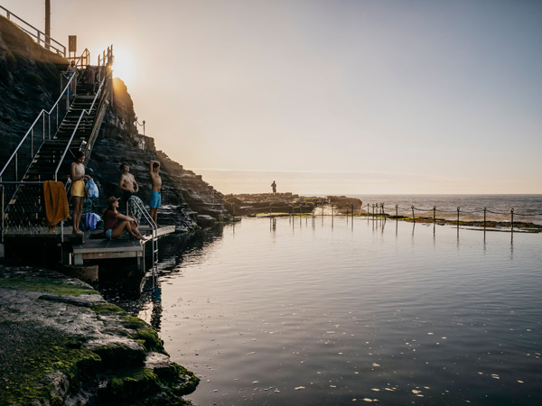 Young people enjoying a swim at Bogey Hole ocean pools in Newcastle at sunrise.