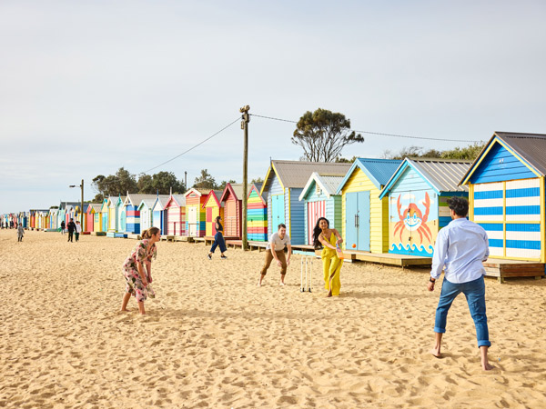 Family playing beach cricket on Brighton Beach in front of Brighton Bathing Boxes