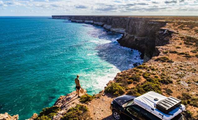 Aerial view of car parked with camper and young man overlooking the Great Australian Bight. Captured while crossing the Nullarbor.