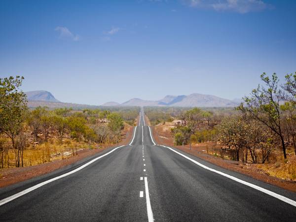 The open road in Kimberly, Western Australia. Straight single lane asphalt road stretching into the distance with mountains in the background. Holiday adventure.