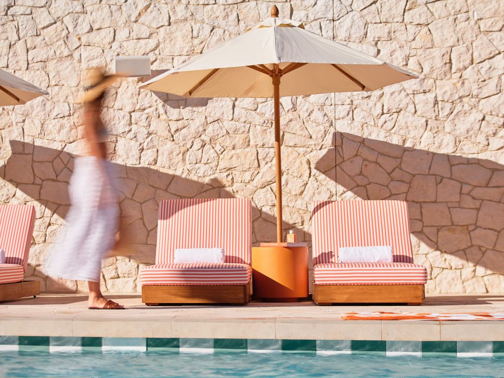 A woman walking past orange striped sun loungers by a pool