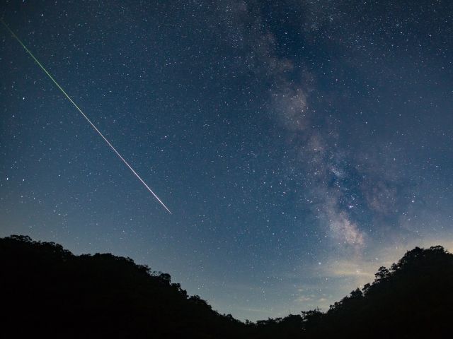 A meteor shoots across the night sky sky leaving a trail of light across the milky way