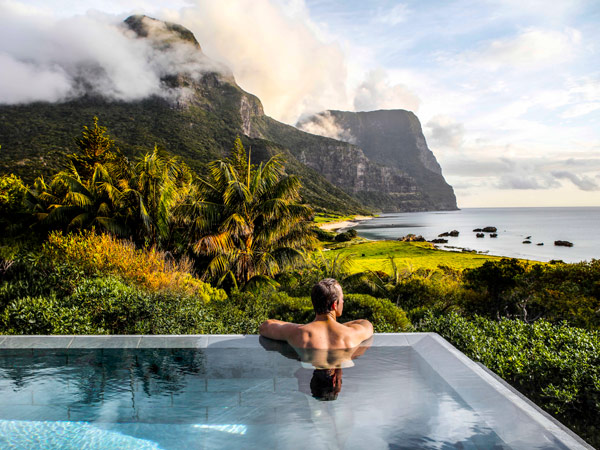 a person dipping in the pool while overlooking views over Lovers Bay and the twin peaks, Mounts Gower and Lidgbird, at Capella Lodge